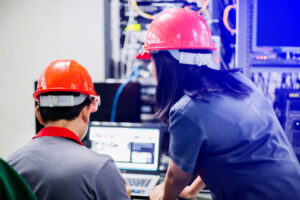 Picture - two engineers working at a computer wearing safety helmets